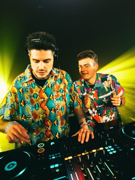 De twee dj's in bonte hemden achter de draaitafels onder geel licht
